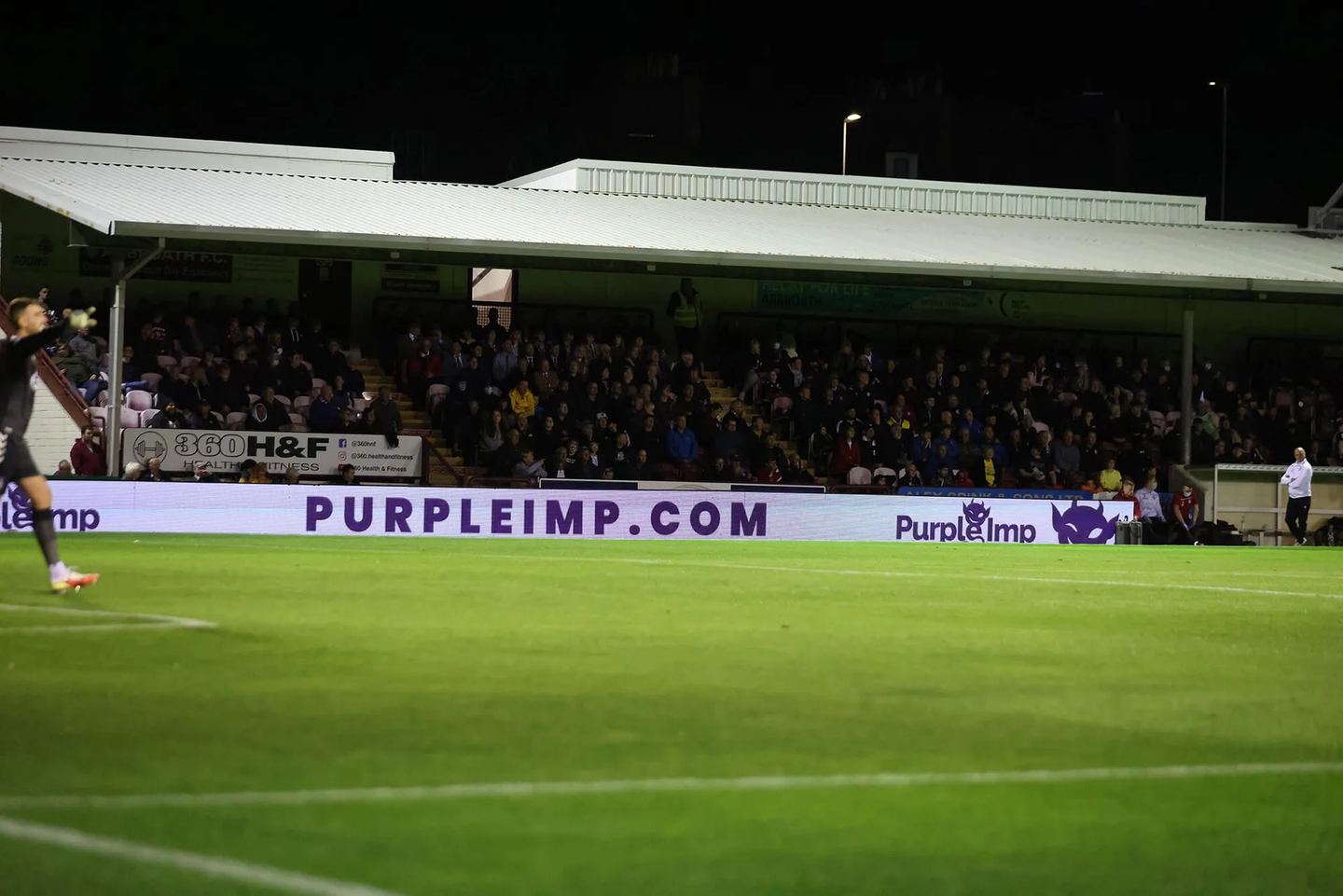 Pitchside LED board reading PURPLEIMP.COM in front of a packed stand